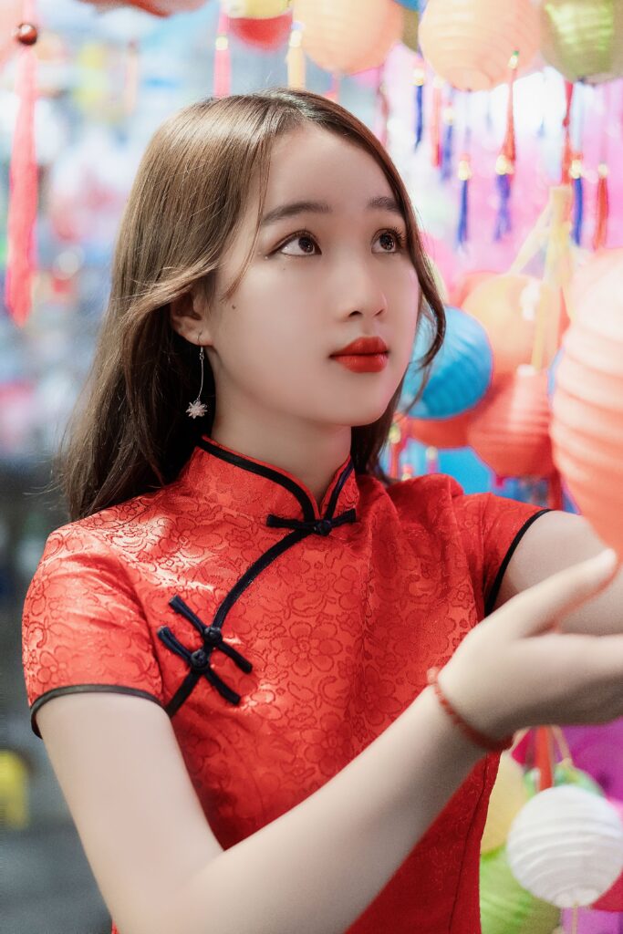 Dreamy Asian female teen with makeup in trendy wear touching colorful lantern while looking up